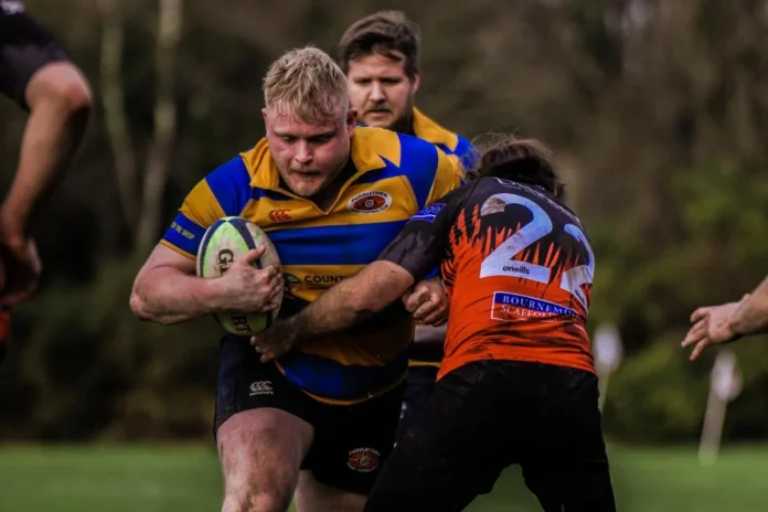 Puddletown rugby player in blue and gold powering through a tackle during a Dorset rugby match